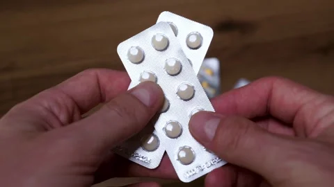 Hands Holding Two Blister Packs of Medicine Tablets Over Wooden Table 库存影片 339197250