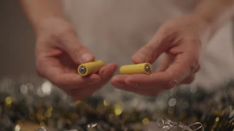 Hands holding two yellow AA batteries, getting ready to insert them into festive Stock Footage 323347969
