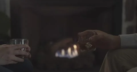 Hands holding whiskey drinks in front of fireplace. Stock Footage 154009358
