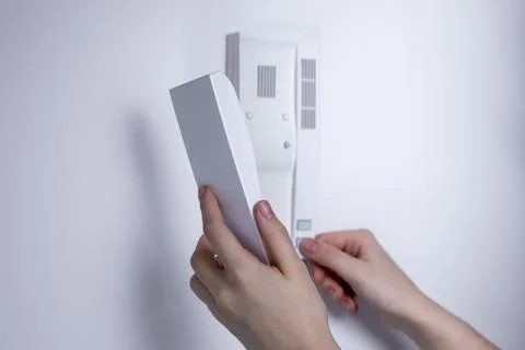 Hands holding a white intercom handset and pressing a button on a wall-mounte Stock Photos