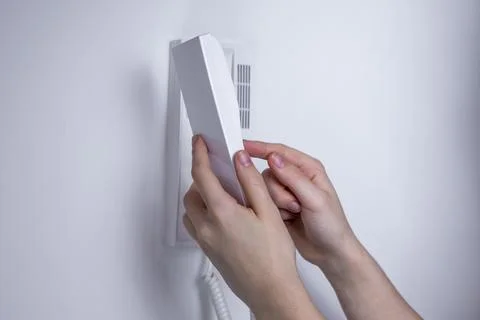 Hands holding a white intercom handset against a wall-mounted device, modern  Stock Photos