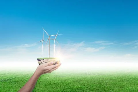 Hands holding wind turbine on grass field against blue sky background. ecolog Foto stock