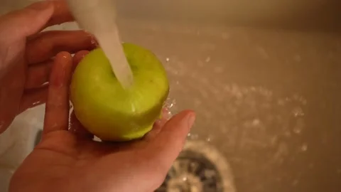Hands of a housekeeper washes an apple in the kitchen sink close-up top view 4K 動画素材 195280632