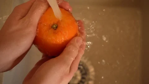 Hands of a housekeeper washes an orange in the kitchen sink close-up top view 4K 库存影片 195280504