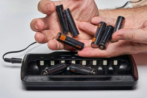 Hands insert AA batteries into black long charger Stock Photos