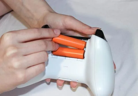 Hands insert batteries into the joystick from the game console. Stock Photos