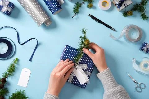 Hands insert a larch twig into a gift. Around it are ribbon, scissors, tape,  Stock Photos