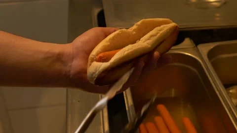 Hands insert sausage into bun making hotdogs in restaurant kitchen 4K 60fps Stock Footage 196988653