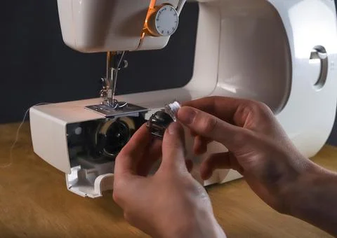 Hands inserting thread into spool or bobbin of sewing machine, starting work, Foto stock