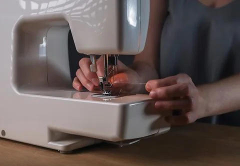 Hands inserting thread through needle hole in sewing machine, details Foto stock
