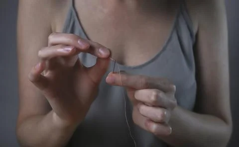 Hands inserting thread through needle hole for sewing. Concept of concentrati Foto stock