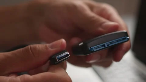 Hands inserting USB micro connector into portable hard drive port in warm indoor Stock Footage 347533512