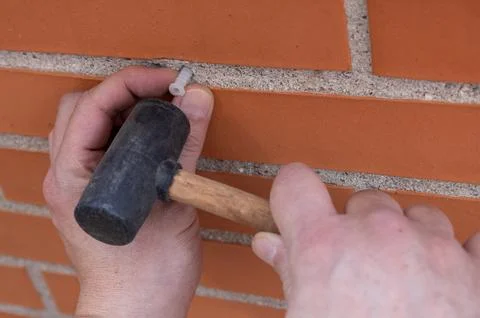 Hands inserting a wall plug into brick with a rubber mallet Stock Photos