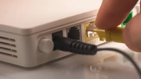 Hands inserting yellow patch cord LAN cable in router Stock-Fotos