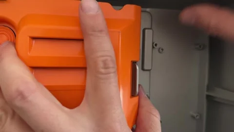 Hands installing or adjusting orange plastic device component, technical Stock Footage 336976940