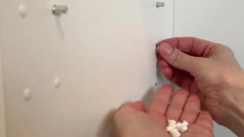 Hands installing plastic hole cover caps in kitchen cabinet shelf pin holes duri Stock Footage 330933568