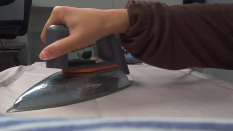Hands ironing laundry with a pile of laundry in the background Stock Footage 276399604