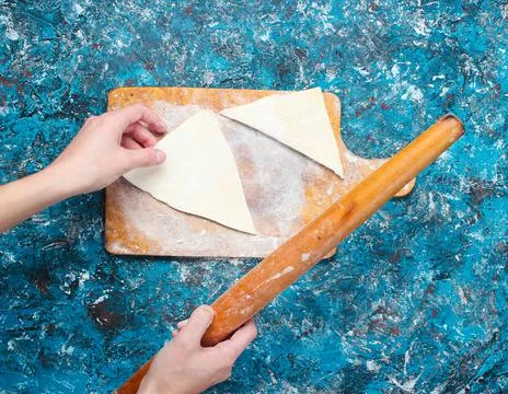 Hands keep rolling pin and roll the dough on blue concrete table. Rustic styl Stock Photos