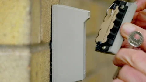 Hands keying in the code to open an outside wall safe then remove a key. Stockbeeldmateriaal 221279401
