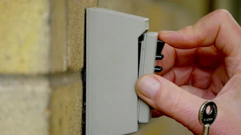 Hands keying in the code to open an outside wall safe then replace a key. Stock Footage 221279649