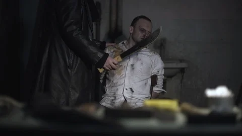 Hands of killer takes machete and comes to tied male hostage and cuts victim. Stock-Footage 86284856