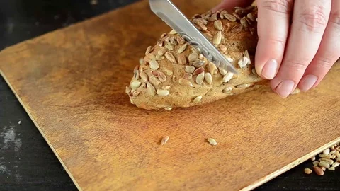 Hands with kitchen knife are cutting grains bread on wooden board. Organic food Stock Footage 113998797