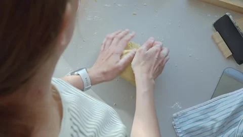 Hands knead dough on floured kitchen counter near smartphone and baking tools Stock Footage 335331977