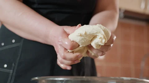 Hands kneading elastic dough above stainless steel mixing bowl inside warm Stock Footage 345657583