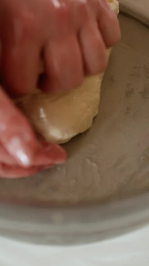 Hands kneading pale dough inside shallow metal bowl in close-up, shaping elastic Stock Footage 345658288