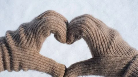 Hands in knitted brown gloves in shape of a heart on  background of white snow. Stock Footage 294492103
