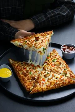Hands lifting two slices of vegetable cheese pizza with melted mozzarella Stock Photos