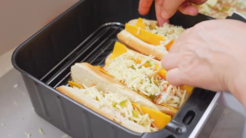 Hands loading cheesy hot dog sandwiches into an air fryer basket in a home .. Stock Footage 347182161