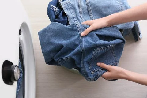 Hands loading denim clothes into washing machine Fotos de archivo