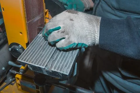 The hands of a locksmith process a part on a belt sander Fotos Stock