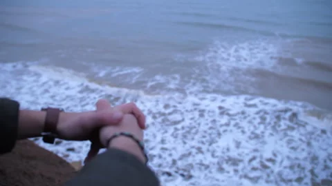 Hands of lone young man sitting on the edge of cliff above dirty sea water Stock Footage 151654507