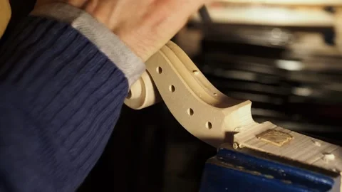 Hands of luthier work on raw violin scroll under a small lamp in Cremona, using Stock Footage 304641736