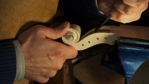 Hands of luthier work on raw violin scroll under a small lamp in Cremona, using Stock Footage 304641852