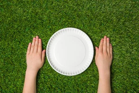 Hands lying near empty paper plate on green grass Stock Photos