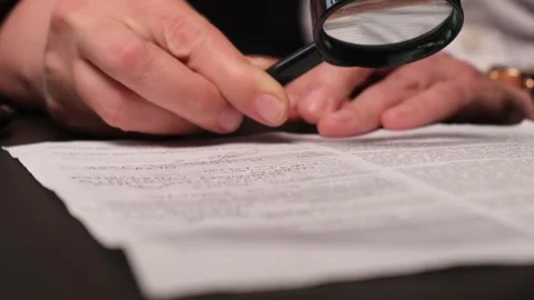 Hands with magnifying glass examining documents or contract before signing or Stock Footage 310841418