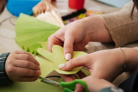 Hands make crafts from colored paper at table Stock Photos