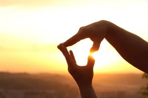 Hands make up a heart shape at sunset. Stock Photos