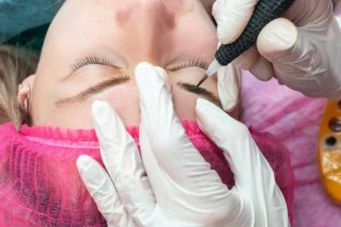 Hands makes permanent makeup eyebrow procedure applying pigment. Stock Photos