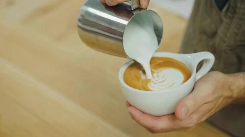 Hands making latte art at a cafe. Making Latte Art by pouring milk into coffee. Stock-Footage 334648533
