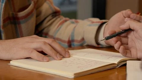 Hands making notes with a pen next to an open book on a cafe table Foto stock
