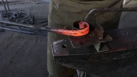 Hands of a male blacksmith bends a red-hot iron into a spiral shape on a large a Stock Footage 120112726