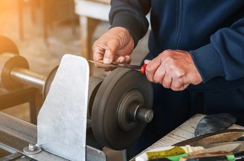 Hands of a male sharpener grinder sharpening knife blade on sharpening machine Stock Photos