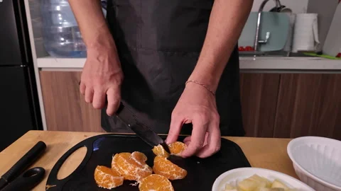 The hands of a man in a apron who is cutting a peeled mandarin into slices. Stock Footage 330063737