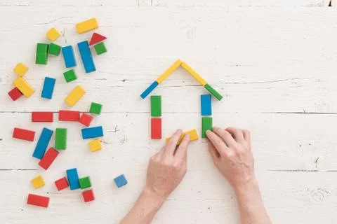 Hands of a man are assembling a house of multi-colored wooden blocks. Early d Stock Photos