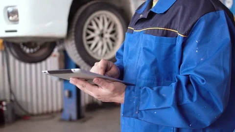 Hands of man car mechanic with tablet with lifted car on background Stock Footage 74905980