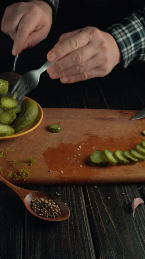Hands of a man in a checkered shirt picking pickled cucumbers on a wooden Stock Footage 336637565